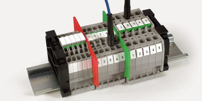 Bloque de borneras Push In de Cabur de color gris montadas sobre riel DIN, mostrando la inserción directa de conductores y puntas de prueba con cables azules, delimitadas por placas de separación rojas y verdes